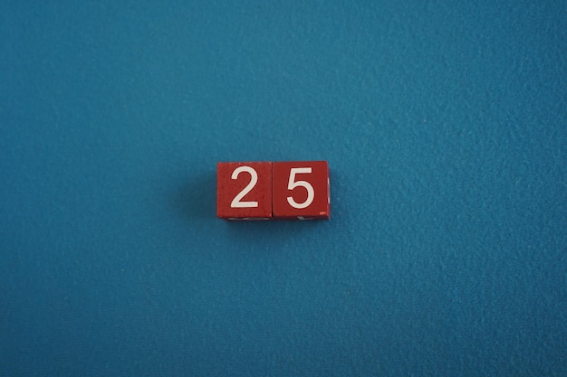 Wooden Viva Magenta cubes with number 25 on blue background closeup top view Concept of date or time White numbers 25 on red cubes velvet background Copy space for text or event Educational cubes
