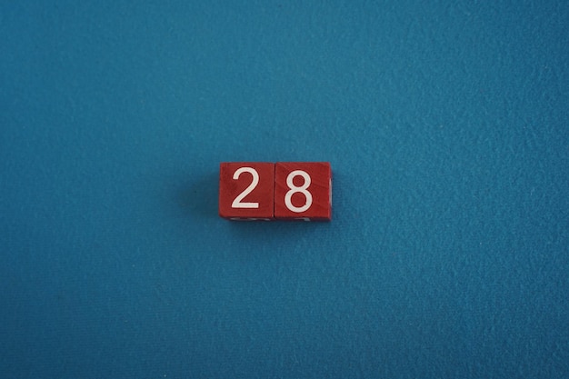 Wooden Viva Magenta cubes with number 28 on blue background closeup top view Concept of date or time White numbers 28 on red cubes velvet background Copy space for text or event Educational cubes