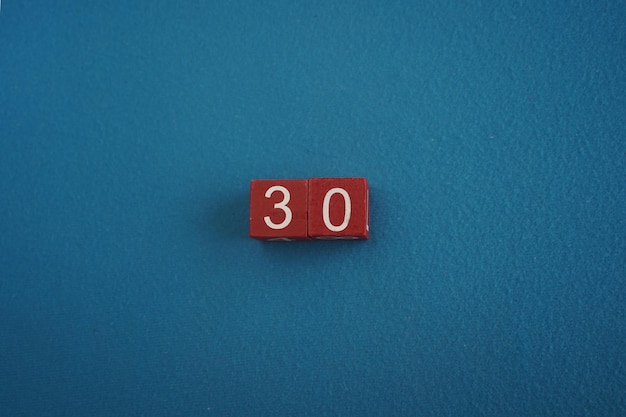Foto cubi in legno viva magenta con il numero 30 su sfondo blu close-up vista superiore concetto di data o ora numeri bianchi 30 su cubi rossi sfondo velluto copia spazio per testo o evento cubi educativi