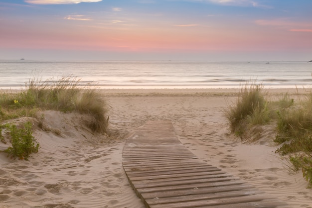 Foto passerella in legno che entra in spiaggia al sorgere del sole