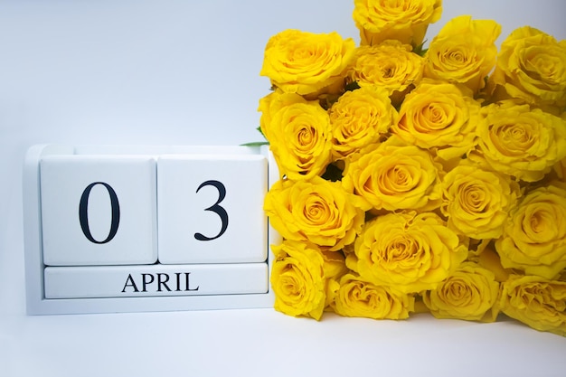 Wooden white calendar April 3 and yellow roses on a white background holidays