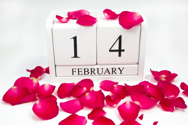 Photo wooden white calendar february 14 on a white background and rose petals lie, holiday, weekend.