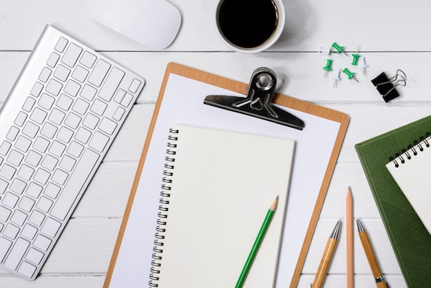 Wooden White office desk table with cup of coffee, Notebook, Pen on it.