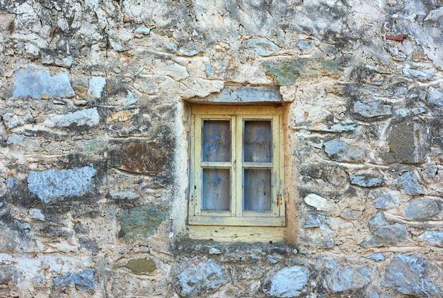 Wooden window on an old rough stone wall farmhouse or ancient house Vintage rustic old fashioned frame on historic village building and background Architecture antique structure with background