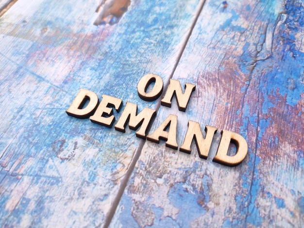 Wooden word on a blue wooden background with the word ON DEMAND