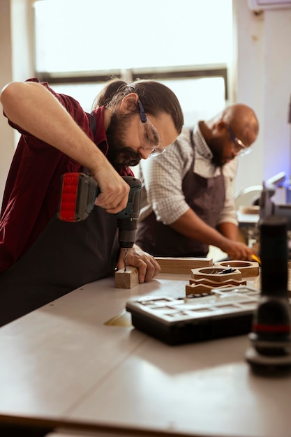 Foto lavoratore del legno in un'officina di assemblaggio che utilizza un trapano elettrico per creare fori per i tasselli