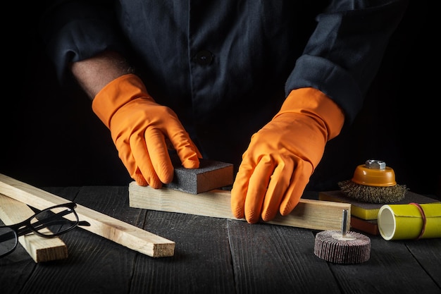 Woodworker cleans a wooden plank with an abrasive tool Hands of the builder closeup during work