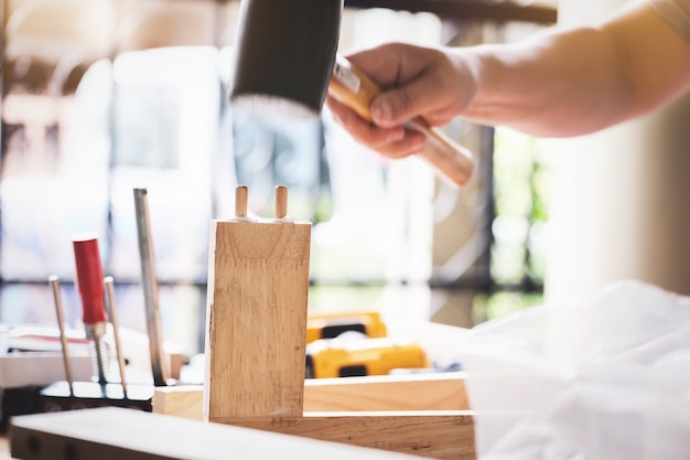 Foto falegname che tiene martello per assemblare i pezzi di legno come ordinato dal cliente