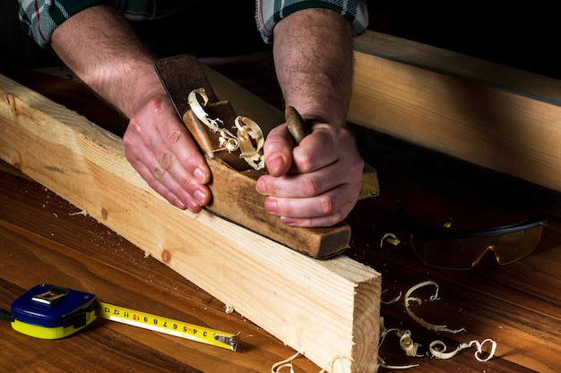 Woodworker using a hand plane to clean up a wooden board. Hands of the master closeup at work.