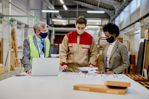 Woodworking foreman and company managers going through design plans at production facility during coronavirus pandemic