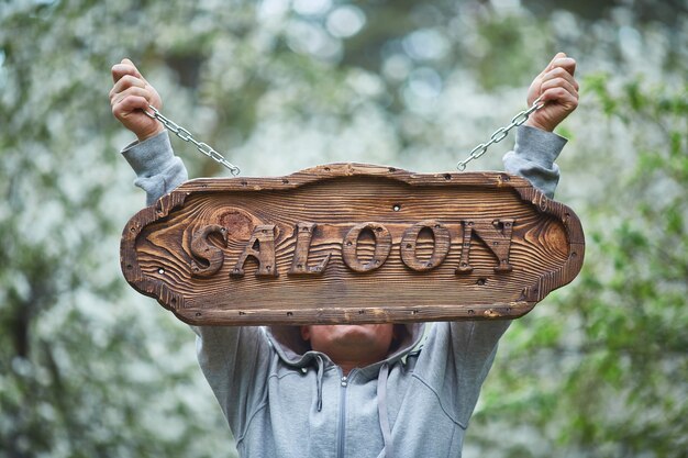 Woodworking. A man holds a sign made of wood with the inscription saloon.