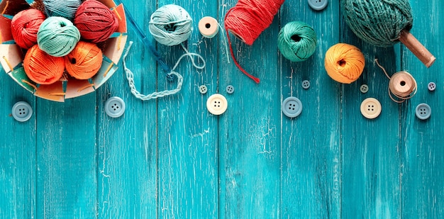 ウールの束、糸のボール、ボタン、コード。ユーズド加工のターコイズウッドに針を掛けて編みます