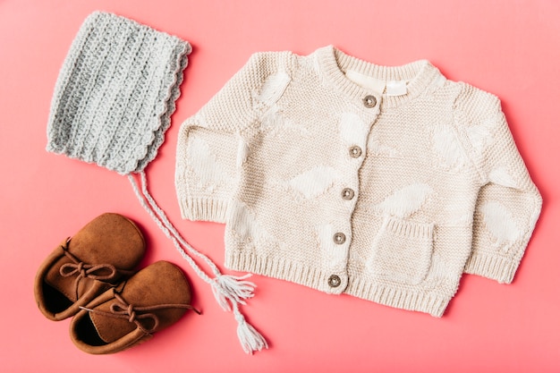 Photo woolen pair of shoes; cap and baby clothing on peach background