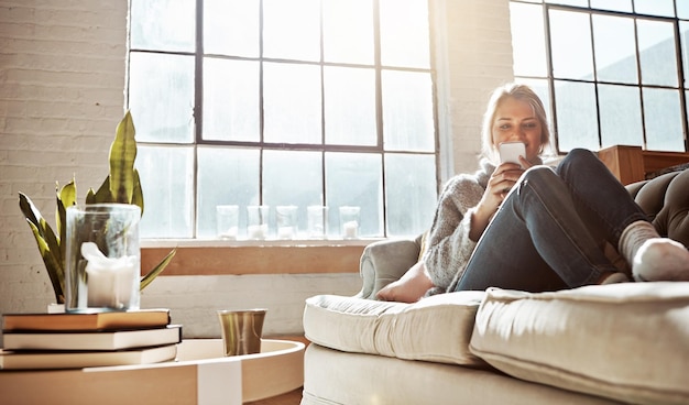 Woonkamer telefoon of ontspannen en een vrouw in haar huis zittend op de bank met de zon schijnt door het raam Weekend sociale media en communicatie met een jonge vrouw die ontspant in haar huis