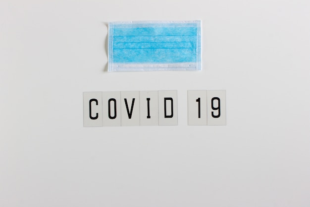 Woord "Covid 19" in zwart op een witte achtergrond met ruimte om te schrijven. Met een coronavirus beschermend masker.