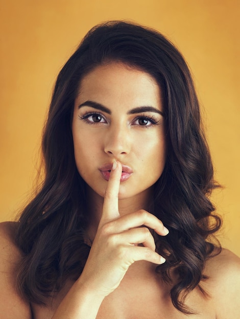 Woorden kunnen haar schoonheid niet beschrijven Shot van een mooie vrouw die poseert met haar vinger op haar lippen tegen een gele achtergrond