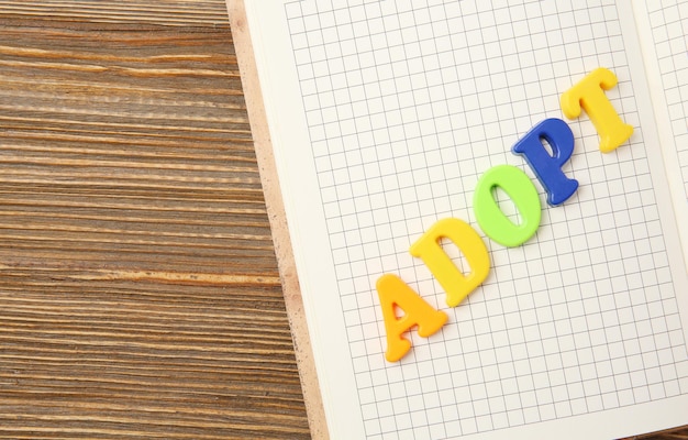 Word ADOPT and open notepad on wooden background closeup