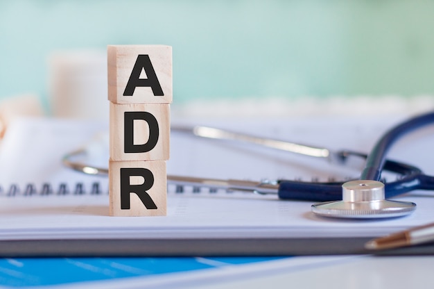 The word adr is written on wooden cubes near a stethoscope on a paper surface