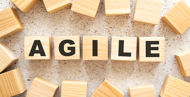 The word AGILE consists of wooden cubes with letters, top view on a light background. Work space.