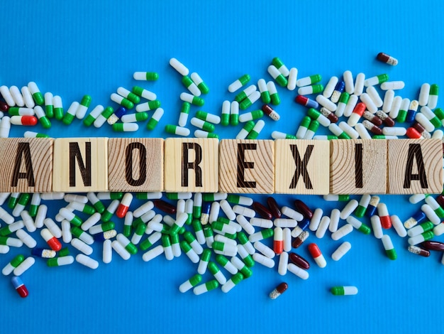 Word anorexia made from wooden cubes with letters next to pills on blue background