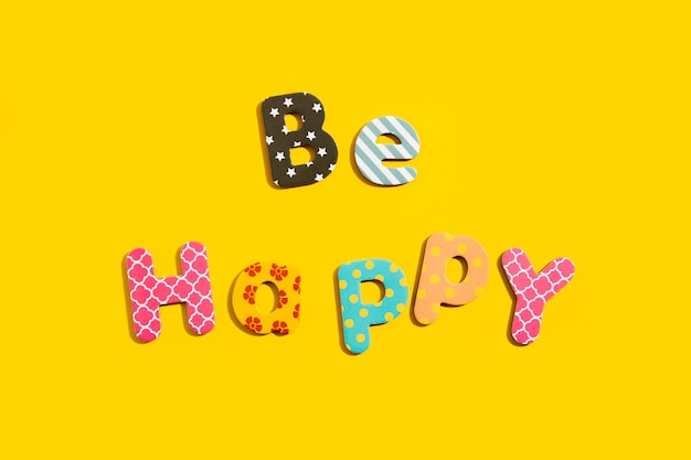 The word Be happy from multicolored letters of the alphabet on a yellow background Top view flat lay