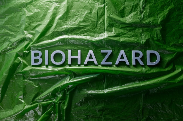 The word biohazard laid with silver letters on green crumpled plastic film background in flat lay composition at center