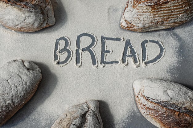 The word bread is drawn in flour between several loaves of bread on a gray background