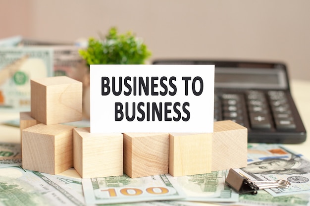the word business to business is written on white paper card near a wooden cubes, bills, calculator on a banknotes 