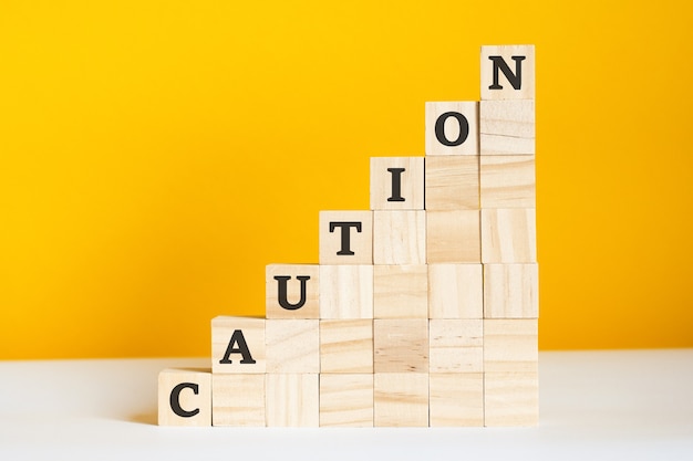 The word caution is written on a wooden cubes. blocks on a bright yellow background. corporate hierarchy concept and multilevel marketing. selective focus.