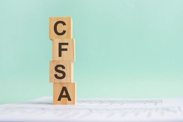 Word CFSA with wood building blocks, light blue background. document with numbers on background, business concept. space for text in right. front view.