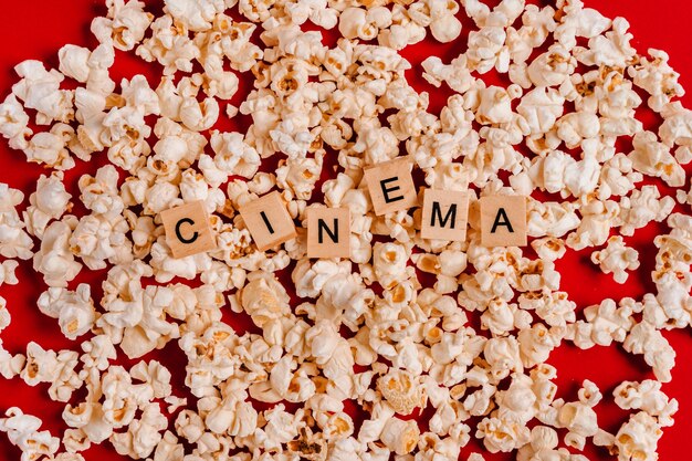 The word CINEMA made of wooden blocks lies on popcorn on a red wall