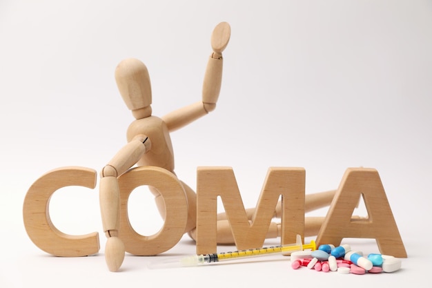 Word Coma made of wooden letters human mannequin and pills on light background closeup