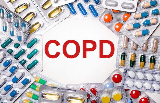 The word COPD is written on a light background surrounded by multi-colored packages with pills. Medical concept