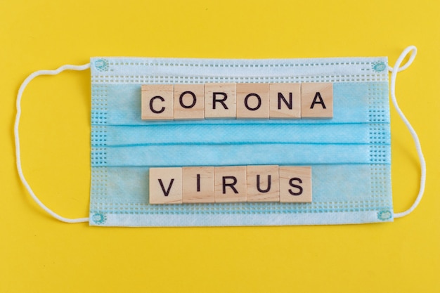 Word Corona Virus gemaakt van houten letters op blauw medisch masker.