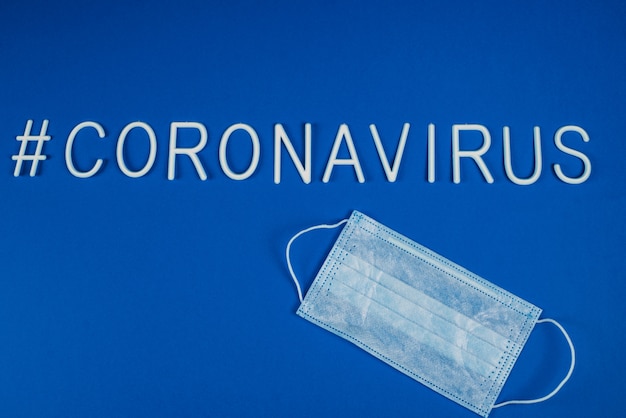 the word coronavirus laid with white letters. Respiratory protection mask next to the word coronavirus. News on social networks. Hashtag. Flat lay, copyspace