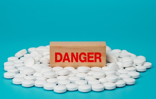 The word DANGED is written on wooden blocks on pile of white pills on blue background. Medical conc