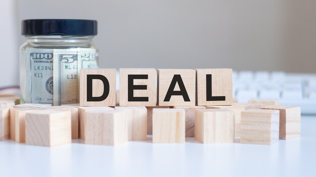 The word Deal on the wooden blocks and a bank with money in the table, business concept