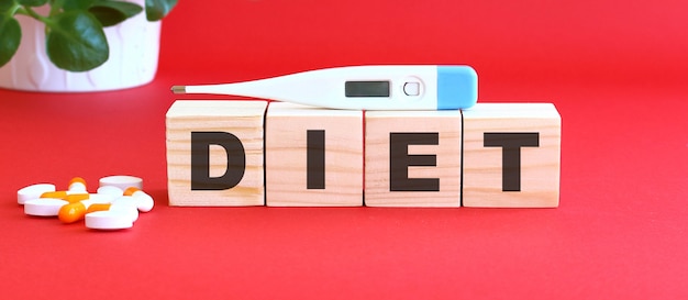 The word DIET is made of wooden cubes on a red with medical drugs.