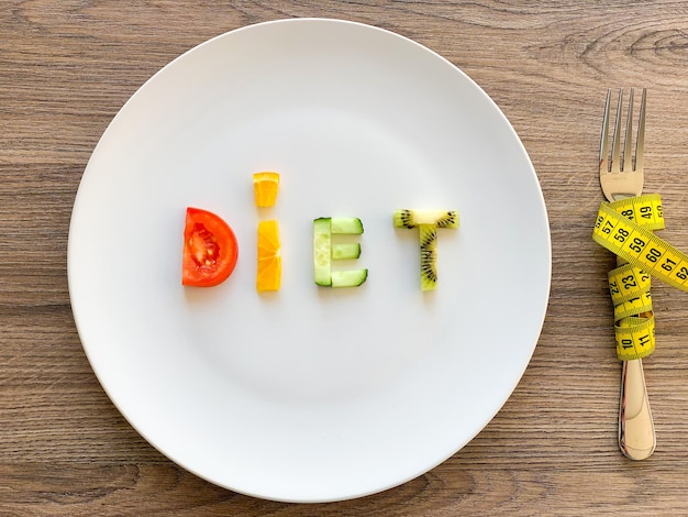 Слово диета из нарезанных овощей в тарелке с измерением на деревянном фоне