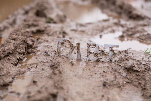 The word dirt composed of silver metal letters on wet clay surface