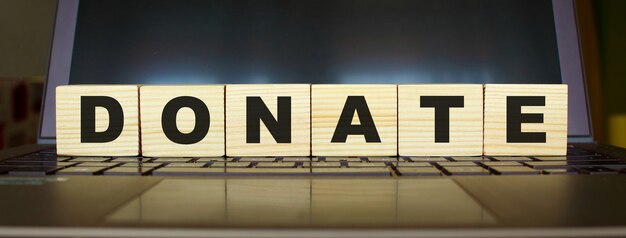 Word DONATE. Wooden cubes with letters isolated on a laptop keyboard. Business Concept image.