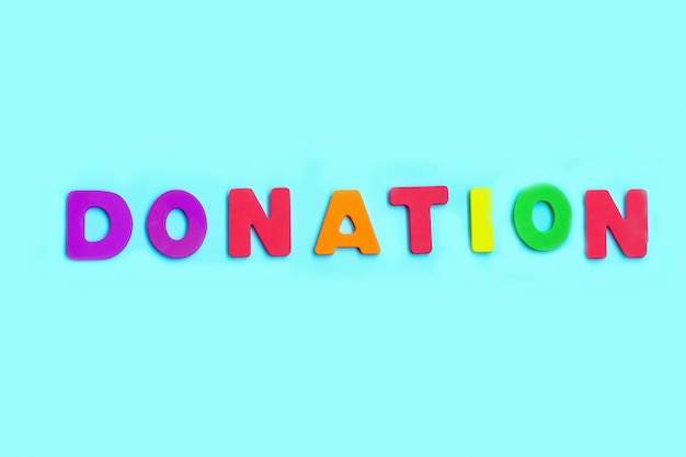 Word DONATION made of colorful letters on blue wall.