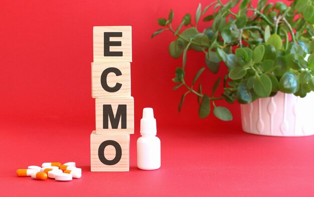 The word ECMO is made of wooden cubes on a red surface with medical drugs.