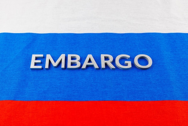 The word embargo laid with silver metal letters on russian tricolor flag in linear perspective