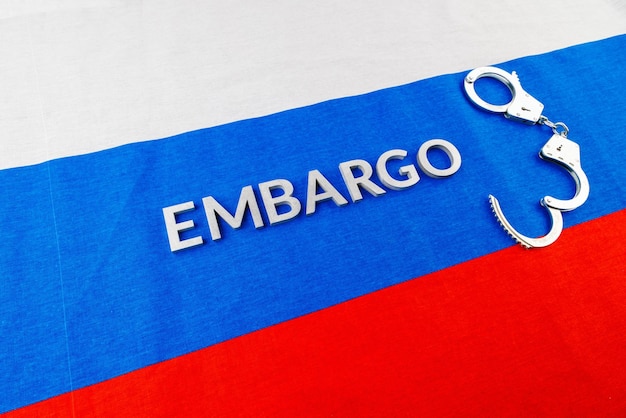 The word embargo laid with silver metal letters on russian tricolor flag with silver handcuffs