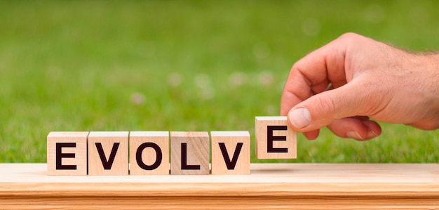 Word evolve written with wooden blocks. Man hand holding wooden cube block with evolve - business word on green lawn background.