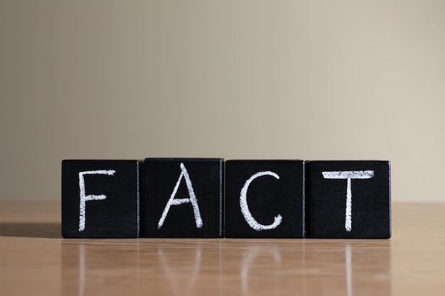 Word FACT made with black cubes on wooden table