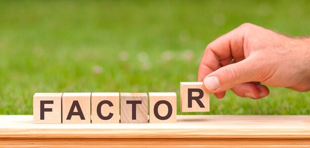 Word factor written with wooden blocks. Man hand holding wooden cube block with factor