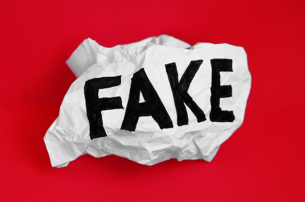 The word fake on crumpled paper on a red background