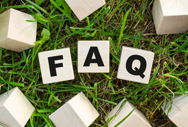 The word FAQ is written on wooden cubes. The blocks are located on green grass with sunlight.